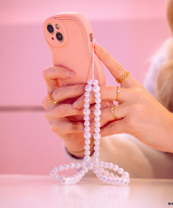 A person with blonde hair holds a pink smartphone adorned with a pearl beaded strap. The person is wearing several gold rings on their fingers, and the background is a soft pink color, showcasing the NAKD Curvy Phone Case - Strawberry by Coconut Lane that offers both style and protection.