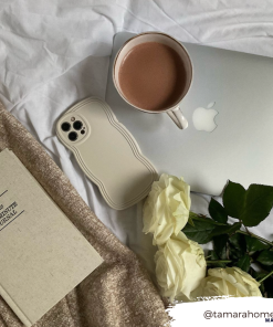 A cozy scene featuring an open MacBook with a cup of coffee on top, a beige iPhone with a highly protective NAKD Curvy Phone Case - Vanilla by Coconut Lane, a book titled 