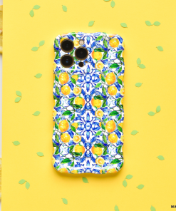 The Wavy Phone Case - Amalfi Lemon by Coconut Lane is showcased on a yellow background. Small green leaf confetti and three lemon slices are placed around it. The case boasts bright blue flowers and yellow Amalfi lemons in a vibrant pattern, providing extra protection for the smartphone.