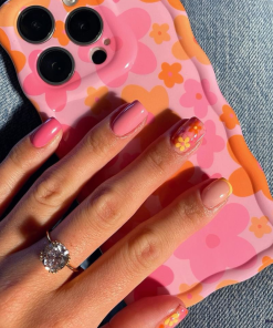 A hand with neatly manicured nails, painted in shades of pink and peach with daisy designs on two nails, holds a smartphone encased in the 