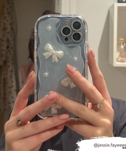 A person with neatly manicured pink nails holds a Pearls & Bows Phone Case from Coconut Lane, featuring a protective clear design embellished with white bows and pearls. The background reveals a blurred bathroom scene with shelves and hanging robes. The Instagram handle @jessie.fayeeee is overlaid on the bottom right corner.