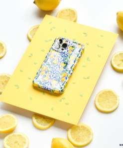 A Coconut Lane Wavy Phone Case - Amalfi Lemon sits on a yellow sheet of paper decorated with green leaf patterns. Surrounding the paper are whole and sliced lemons, creating a bright and cheerful scene.