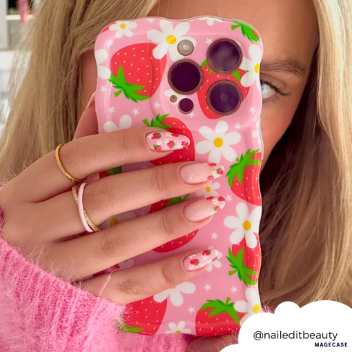 Close-up of a person holding a phone with Coconut Lane's Wavy Phone Case - Berry Cute Strawberry, featuring an adorable strawberry and daisy-themed design. The phone partially covers their face, perfectly matching their strawberry and floral nail art. They are wearing a pink sweater and gold rings. "@naileditbeauty" is displayed in a cloud shape.
