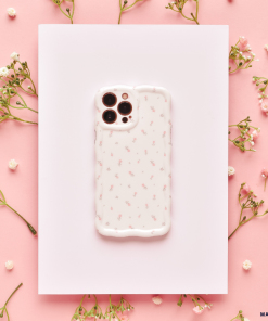 A smartphone encased in Coconut Lane's Wavy Phone Case - Ditsy Floral White lies on a white rectangular sheet, surrounded by delicate sprigs of small white flowers on a pink background. The overall aesthetic is soft and feminine.