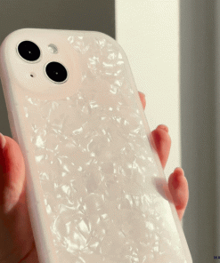 A hand holds a smartphone with a Moonstone Pink Phone Case by Coconut Lane. The phone has two rear camera lenses and is positioned in front of a bright window, emphasizing the glossy finish of the protective phone case.