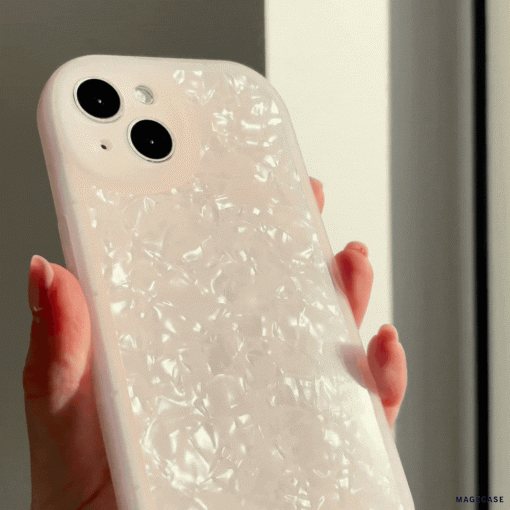 A hand holds a smartphone with a Moonstone Pink Phone Case by Coconut Lane. The phone has two rear camera lenses and is positioned in front of a bright window, emphasizing the glossy finish of the protective phone case.