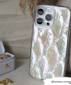 A silver iPhone with a gleaming Real Natural Shell Phone Case - White from Coconut Lane rests on a surface beside an open white box holding gold jewelry. The backdrop features dried foliage. The Instagram handle 