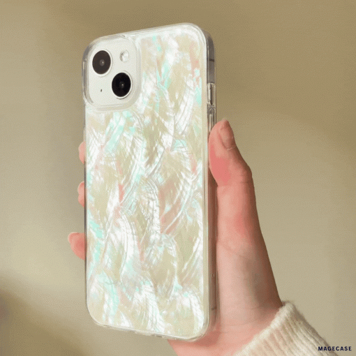 A hand holding an iPhone with Coconut Lane's Real Natural Shell Phone Case - White, which features a glossy, iridescent finish and a subtle feather-like pattern. The background is softly blurred. The case has a luminous, pearlescent sheen with hints of pink, blue, and green reflecting off its surface.
