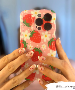 Close-up of hands holding an extra protective Coconut Lane Wavy Phone Case - Berry Cute Strawberry, featuring a pink design with strawberries and white flowers. The person's nails are painted white with red strawberry designs. Instagram handle @lily_erickson is in the bottom right corner.