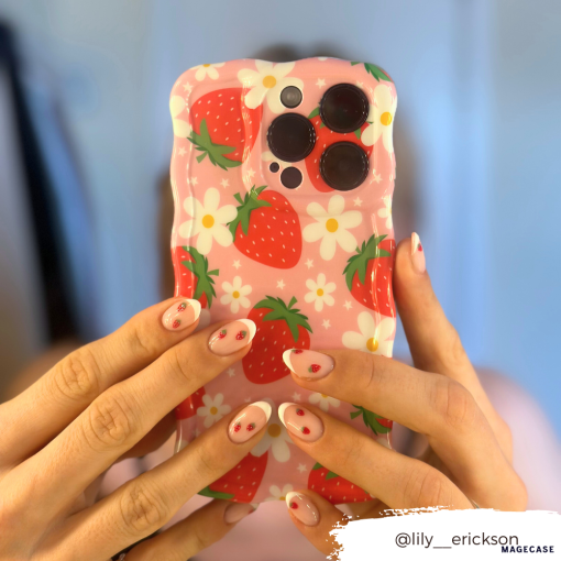 Close-up of hands holding an extra protective Coconut Lane Wavy Phone Case - Berry Cute Strawberry, featuring a pink design with strawberries and white flowers. The person's nails are painted white with red strawberry designs. Instagram handle @lily_erickson is in the bottom right corner.