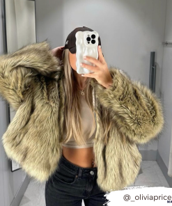 A person takes a mirror selfie in a well-lit room. They are wearing a tan crop top and black pants, topped with a large, fluffy, tan fur coat. They also have long, blonde hair and a black baseball cap. The Instagram handle @_oliviapricee is visible in the corner along with their 3D Pearl Phone Case - White from Coconut Lane.
