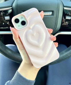 A person with pink nail polish holds a smartphone adorned with Coconut Lane's Melting Heart Phone Case in Peony Pink. Seated in the driver's seat of a vehicle, the steering wheel and dashboard are visible in the background, highlighting the chic allure of their phone case featuring a raised heart design.