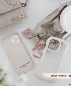 A stylish flat lay featuring a beige Jacquemus bag, a white coffee cup with a lid, two highly protective iPhone 15 cases (one beige and one Coconut Lane Curvy Phone Case in cream), pink beaded accessories, and a tag labeled 