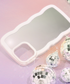A sleek and stylish Curvy Mirror Phone Case - Cream from Coconut Lane lies on a pink and purple gradient background. Surrounding the curvy mirror phone case are several shiny, mirrored disco ball ornaments of varying sizes, reflecting light and casting a festive, glamorous feel to the image.
