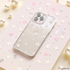 A smartphone adorned with the Mini White Bows Phone Case from Coconut Lane rests on a glittery pastel background, enhanced by scattered pink and silver star-shaped confetti and pearls. The phone’s triple camera setup is elegantly visible, contributing to a whimsical and sophisticated aesthetic.