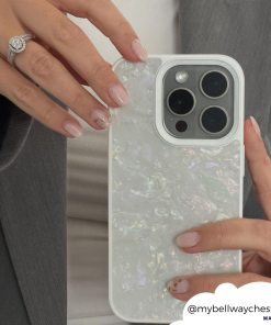 A person with a grey blazer is holding a Mother of Pearl Phone Case by Coconut Lane in their left hand. Their nails are painted in a light, natural color with minimalist designs. There is a diamond ring on their left ring finger, and the username 