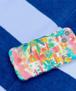 A Wavy Phone Case – Portofino Dreams by Coconut Lane, showcasing a colorful and vibrant Italian seaside design with palm trees and houses, rests on a surface adorned with blue and white stripes. The extra protective case includes cutouts for dual cameras and a flash.
