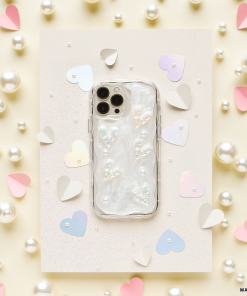 An iPhone15 with a Coconut Lane's Pearly Hearts Phone Case - Clear lies on a sparkly white surface. The background features scattered white pearls and cut-out heart shapes in pastel colors, including pink, lilac, and beige.