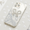 A smartphone encased in the Coconut Lane Diamante Bow Phone Case, which boasts a sparkling bow decoration, rests on a light gray surface. This distinctive phone case infuses an element of elegance, while the background is sprinkled with scattered white, star-like confetti. The phone's camera lenses are clearly visible, prominently situated at the top left corner.