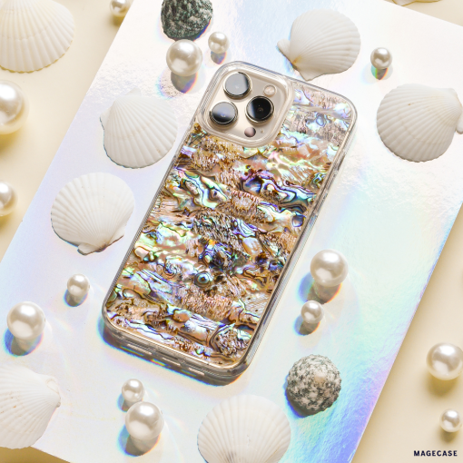 The Coconut Lane Real Natural Shell Phone Case - Black, showcasing an exquisite abalone shell-patterned design, is elegantly displayed on a reflective holographic surface. Surrounded by white seashells, spherical pearls, and textured grey stones, it crafts an immersive marine-inspired aesthetic.