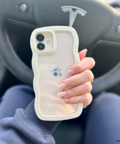 A person with manicured nails holds an iPhone encased in the highly protective Curvy Phone Case - Cream by Coconut Lane, featuring a wavy design. The steering wheel adorned with the Tesla logo is visible in the background, indicating they are seated in the driver's seat of a Tesla vehicle.