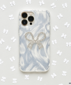 A Coconut Lane Diamante Bow Phone Case, featuring a marbled light grey design and adorned with a diamante bow decoration, is surrounded by small white paper stars on a light grey background.