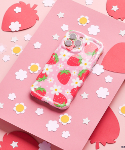 A Coconut Lane Wavy Phone Case - Berry Cute Strawberry with a delightful strawberry pattern and white flowers rests on a pink surface, surrounded by cut-out paper shapes of strawberries and flowers. The background includes larger pink strawberry shapes and smaller white flower shapes scattered around.