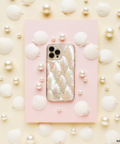A white iPhone adorned with Coconut Lane's Real Natural Shell Phone Case is set on a pastel pink rectangular card, surrounded by white seashells and pearls, all against a cream-colored background. This arrangement creates a marine-themed aesthetic with a soft, elegant feel.