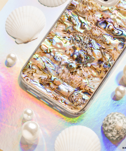 A smartphone with a reflective Coconut Lane Real Natural Shell Phone Case in Black lies on a pastel-colored, iridescent surface. Surrounding the phone are authentic durable shells and variously sized pearls, enhancing the aquatic theme.