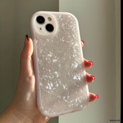 A hand with red-painted nails holds a Coconut Lane Moonstone Pink Phone Case for the iPhone15. The iridescent, protective case features a textured and translucent design that catches the light, creating a shimmering effect. The modestly lit background highlights the intricate details of the phone case.
