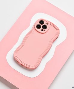 A strawberry-colored smartphone with a matching wavy-edged case rests on a pink and white abstract-patterned surface. The matte finish of the Coconut Lane NAKD Curvy Phone Case - Strawberry adds an elegant touch, while its highly protective design ensures the three-lens rear camera setup remains safe and secure.