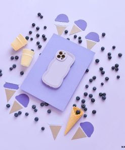 A pastel purple phone in a Coconut Lane NAKD Curvy Phone Case - Blueberry is placed on a light purple surface, surrounded by blueberries and cutouts of ice cream cones. Two small empty waffle cones and two yellow disposable cups also accompany the arrangement, all in a visually pleasing layout.