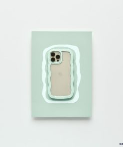 A modern iPhone 15 with a beige back and three camera lenses is placed on a pastel green rectangular surface. The surface features an irregular white and mint green outline, complementing the minimalistic setting. It is protected by the Mint Curvy Phone Case from Coconut Lane.