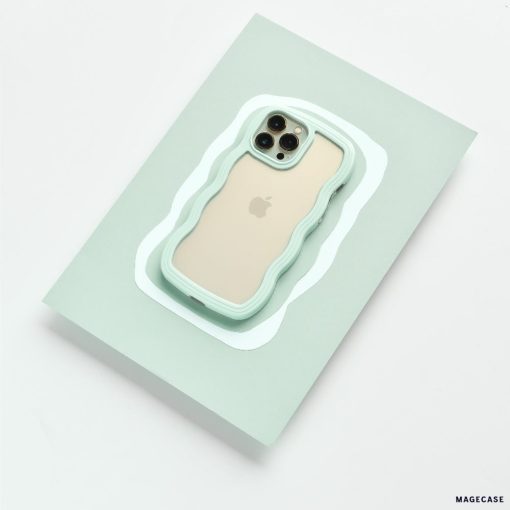 A gold iPhone, identified as an iPhone15, is encased in the rugged and wavy-edged Coconut Lane Curvy Phone Case in Mint. It's placed on a light green rectangular surface with a precise cutout that fits the phone perfectly. The camera lenses and Apple logo remain visible through the protective case.