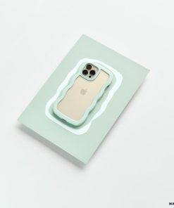 A beige iPhone 15 with a triple camera setup is encased in a Curvy Phone Case - Mint by Coconut Lane. It is placed on a light green rectangular surface, against a clean, white background.