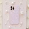 A smartphone encased in a Moonstone Pink Phone Case by Coconut Lane, glossy and textured, rests on a surface adorned with various sizes of pearls. The camera lenses are visible at the top left of the phone. The background features a slightly glittery pastel finish, adding an elegant touch.