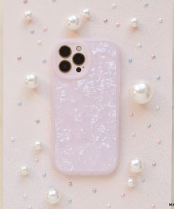 A smartphone encased in a Moonstone Pink Phone Case by Coconut Lane, glossy and textured, rests on a surface adorned with various sizes of pearls. The camera lenses are visible at the top left of the phone. The background features a slightly glittery pastel finish, adding an elegant touch.