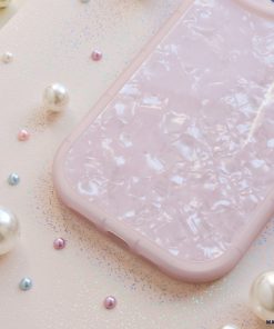 A Moonstone Pink Phone Case from Coconut Lane with a pearlescent, mosaic-like design placed on a glittery pink surface. Surrounding the protective phone case are scattered pearls of varying sizes, adding a touch of elegance to the scene.