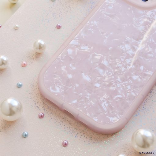 A Moonstone Pink Phone Case from Coconut Lane with a pearlescent, mosaic-like design placed on a glittery pink surface. Surrounding the protective phone case are scattered pearls of varying sizes, adding a touch of elegance to the scene.