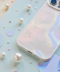 A pastel-colored smartphone with Coconut Lane's Mother of Pearl Phone Case lies on a light blue background adorned with various sizes of glossy white and pastel-colored beads and circular holographic cutouts.