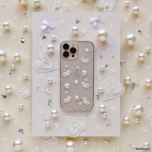 A Coquette Dreams Phone Case by Coconut Lane for the iPhone 15 lies in the center of a beige background adorned with pearls, lace hearts, and tiny bows. The intricate details of this extra protective case and the surrounding decorations exude a delicate, elegant aesthetic.