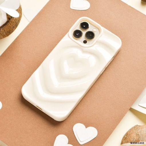 A Melting Heart Phone Case - Coconut Cream by Coconut Lane, with its smooth, pale beige case featuring a raised, 3D heart design, lies on a piece of brown paper. Surrounding the phone are small white heart-shaped cutouts and halved coconuts. The background showcases cream-colored and various brown tones.