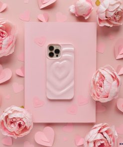 A Melting Heart Phone Case - Peony Pink by Coconut Lane lies on a larger pink rectangle, surrounded by pink paper hearts and pink peonies. The overall pink theme creates a soft, romantic aesthetic.