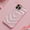 A Coconut Lane Melting Heart Phone Case in Peony Pink encases a smartphone resting on a pink surface. Multiple paper hearts are scattered around, enhancing the romantic and playful theme. The background features an array of pink shades and textures.