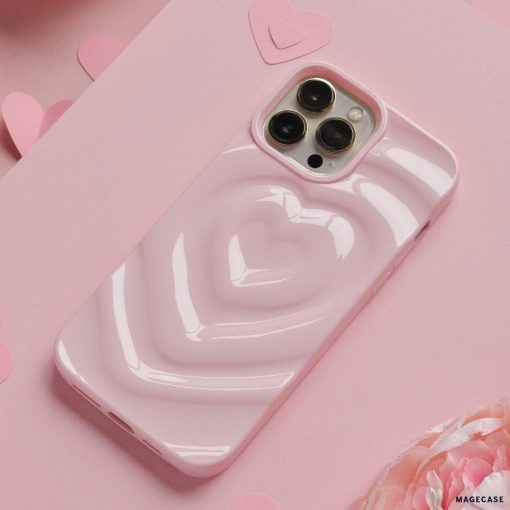 A Coconut Lane Melting Heart Phone Case in Peony Pink encases a smartphone resting on a pink surface. Multiple paper hearts are scattered around, enhancing the romantic and playful theme. The background features an array of pink shades and textures.