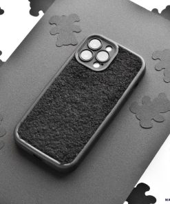 A black Cosy Teddy Phone Case from Coconut Lane is displayed on a grey surface. The protective phone case has cut-outs for the camera and buttons. The background features scattered black cloud-shaped cut-outs on white paper, creating a contrasting pattern.