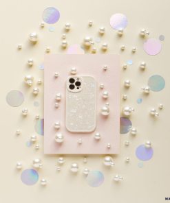 A smartphone in the Moonstone Pearl Phone Case by Coconut Lane, featuring a sparkly, translucent design, is placed on a light pink rectangular paper. Surrounding it are scattered white pearls and iridescent circular confetti on a light beige background, creating a decorative and elegant arrangement.