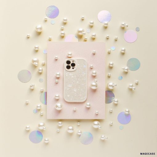 A smartphone in the Moonstone Pearl Phone Case by Coconut Lane, featuring a sparkly, translucent design, is placed on a light pink rectangular paper. Surrounding it are scattered white pearls and iridescent circular confetti on a light beige background, creating a decorative and elegant arrangement.