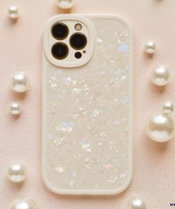 A smartphone protected by the Coconut Lane Moonstone Pearl Phone Case, showcasing an iridescent shell design, is placed on a light pink glittery surface. The phone, potentially an iPhone15 case model, features three rear cameras and is encircled by small and large pearl-like decorative spheres.