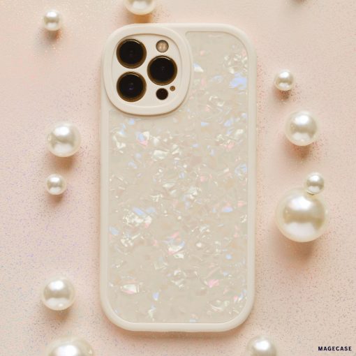 A smartphone protected by the Coconut Lane Moonstone Pearl Phone Case, showcasing an iridescent shell design, is placed on a light pink glittery surface. The phone, potentially an iPhone15 case model, features three rear cameras and is encircled by small and large pearl-like decorative spheres.
